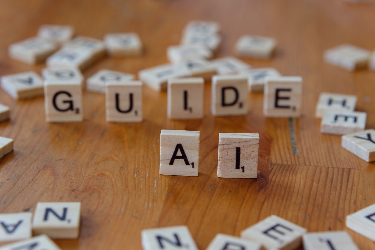Home Scrabble letters spelling 'GUIDE' and 'AI' on a wooden surface, suggesting direction and technology.